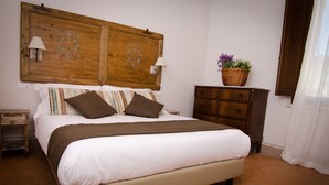 A bedroom with a large bed, wooden headboard, bedside lamps, a dresser, and a basket with flowers. - Dimora Dell'Erbe (Montepulciano)