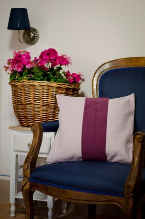 Ein Stuhl mit blauer Kissenauflage und einem dekorativen Kissen, ein Korbwicker-Korb mit Blumen und eine Wandleuchte.