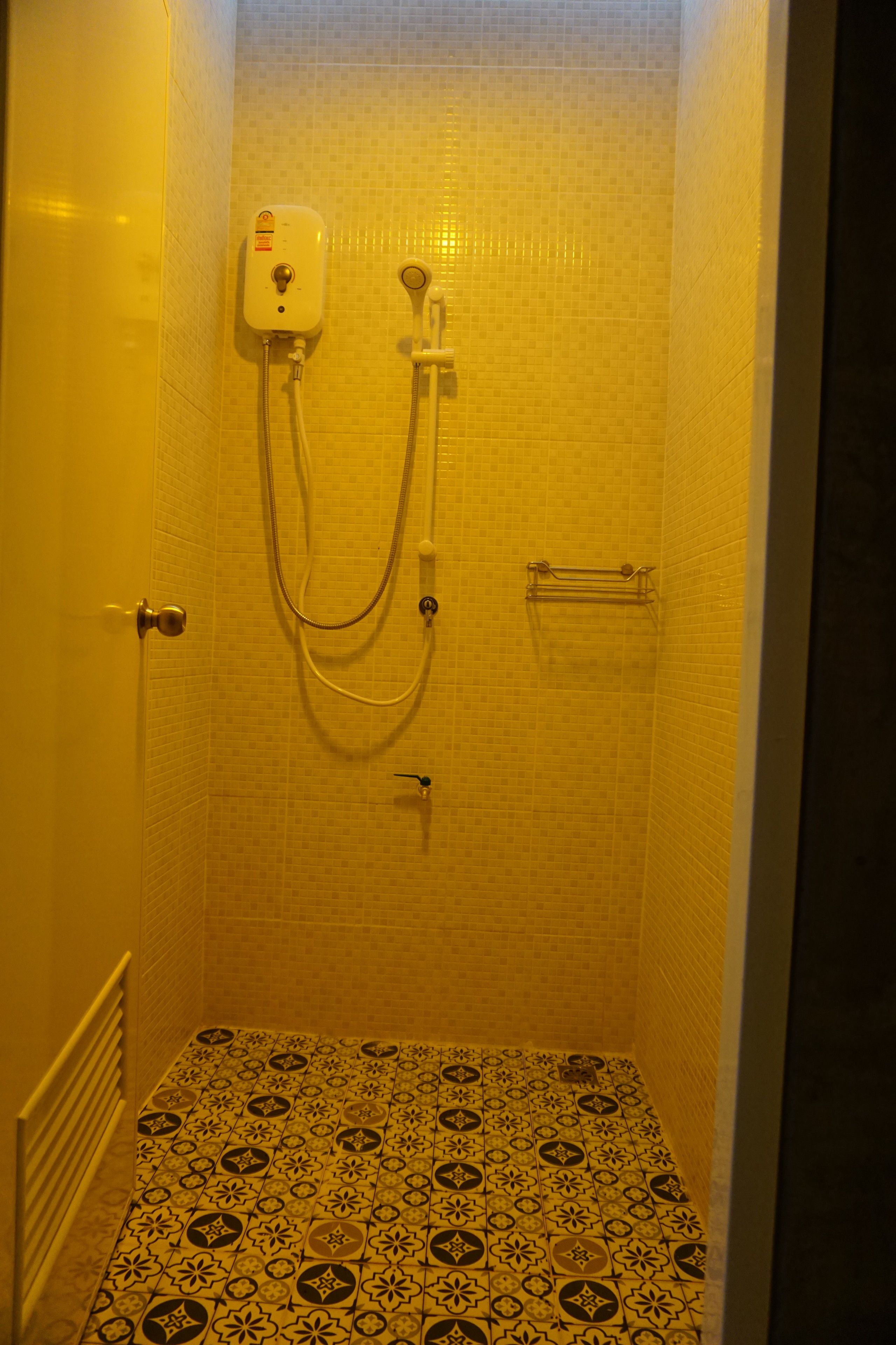 A small, enclosed shower area with a tiled floor and walls, a handheld showerhead, and a control panel.