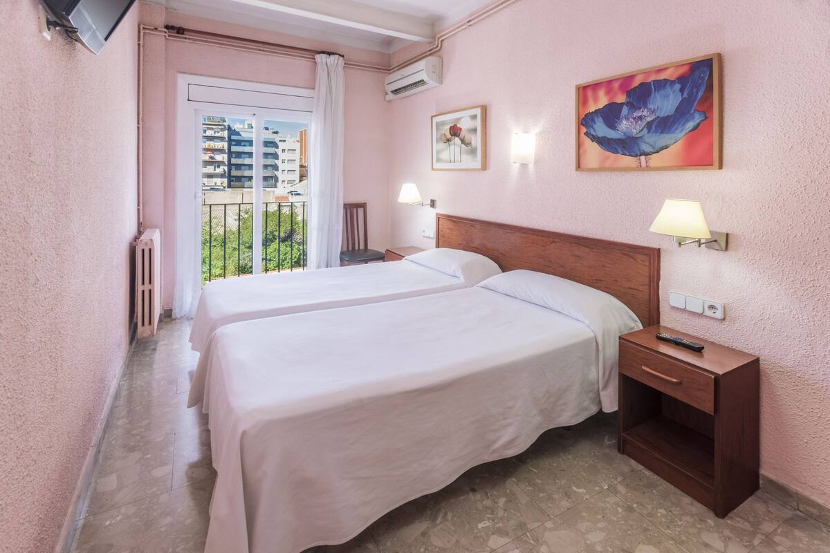 A hotel room with two beds, a balcony, a TV, and artwork on the walls.