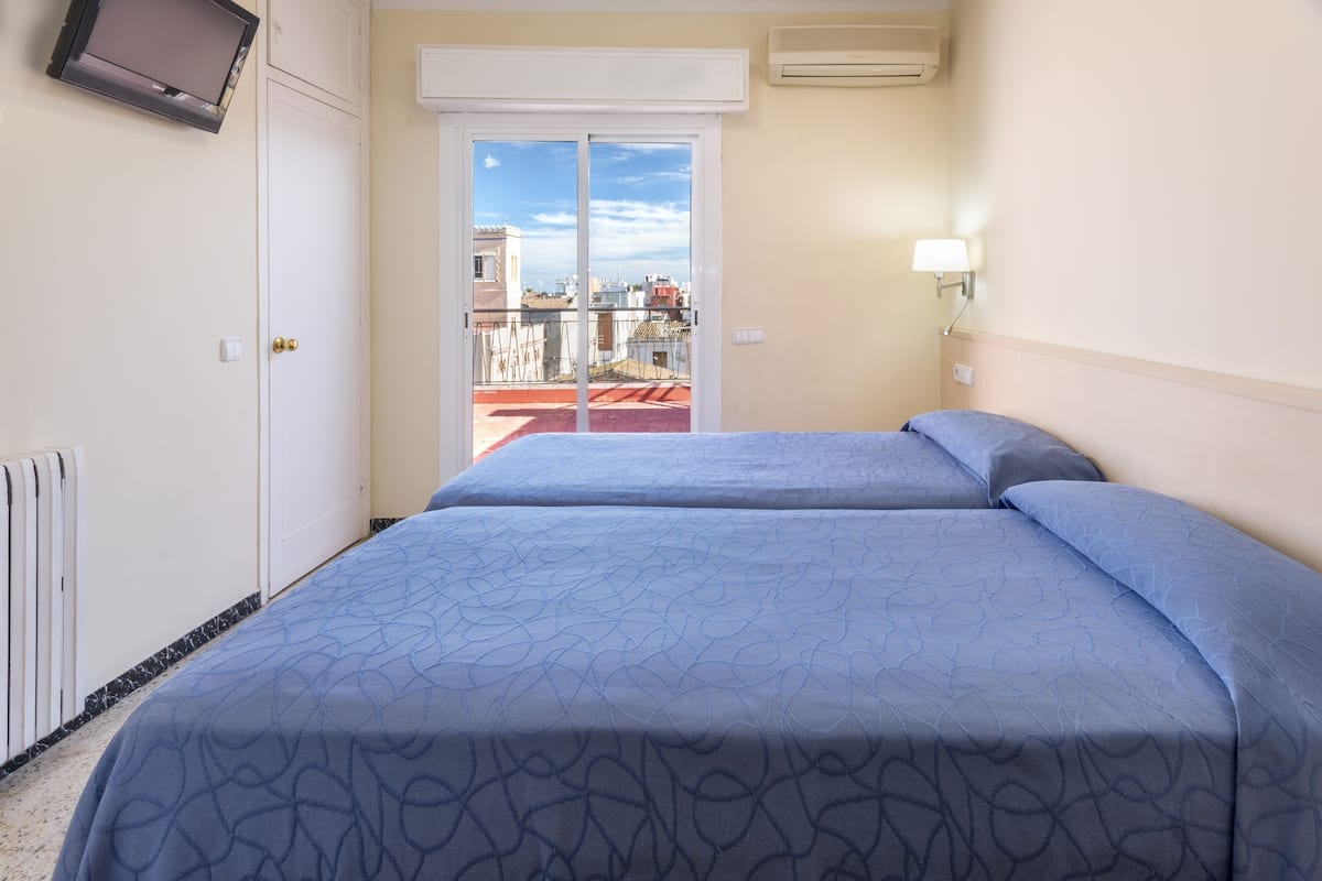 A hotel room with two beds, a sliding door to a balcony, a television mounted on the wall, and an air conditioning unit.