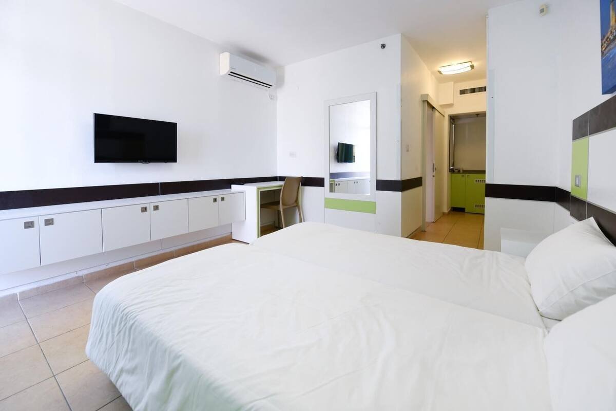 A hotel room with a large bed, a desk with a chair, a flat-screen TV mounted on the wall, and a bathroom visible through an open door.
