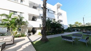 A modern building with multiple balconies, a grassy courtyard with outdoor seating, and palm trees. - HI Tel Aviv (Tel Aviv)