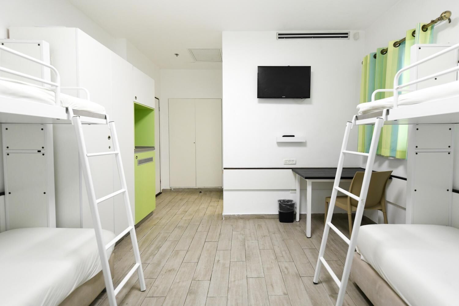 Habitación tipo dormitorio con literas, un escritorio, una silla, un televisor y un cubo de basura.