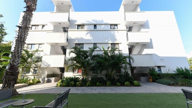 A modern multi-story building with balconies, surrounded by well-maintained greenery and a grassy area with outdoor seating. - HI Tel Aviv (Tel Aviv)