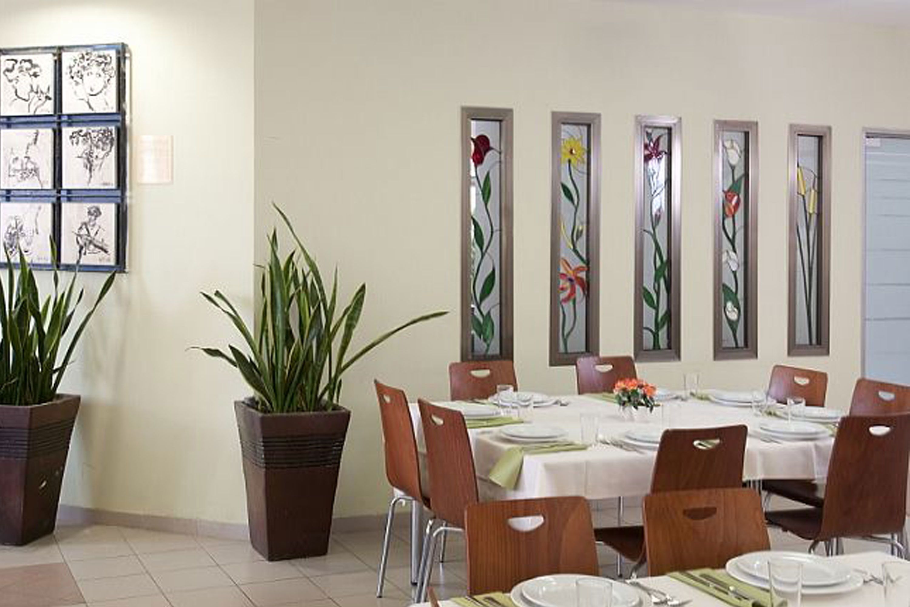 A dining area with tables set for six, potted plants, and artwork on the wall.