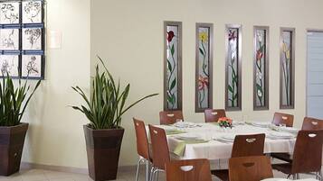 A dining area with tables set for six, potted plants, and artwork on the wall.