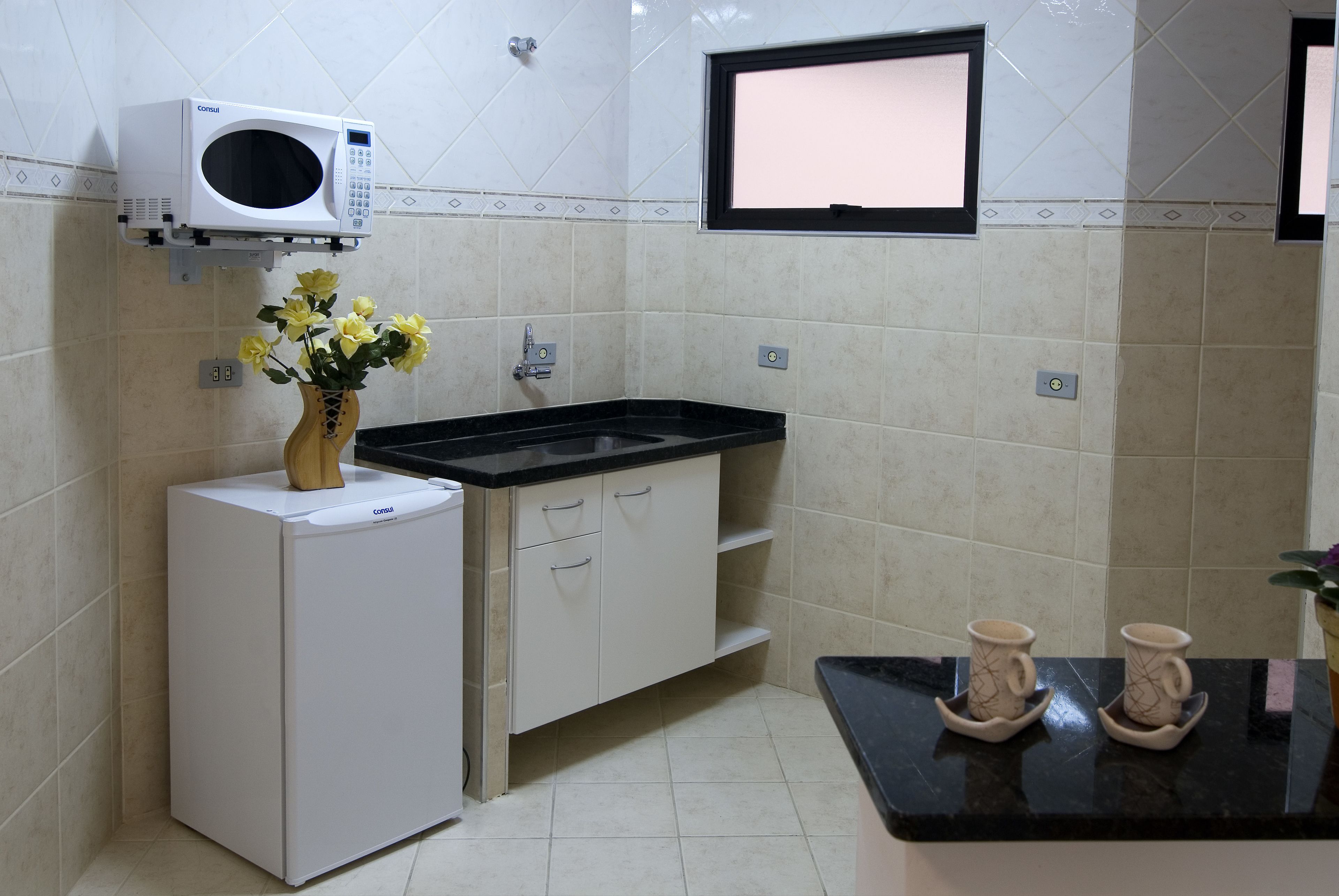 Una cocina compacta con microondas integrado, un lavamanos y una pequeña encimera.