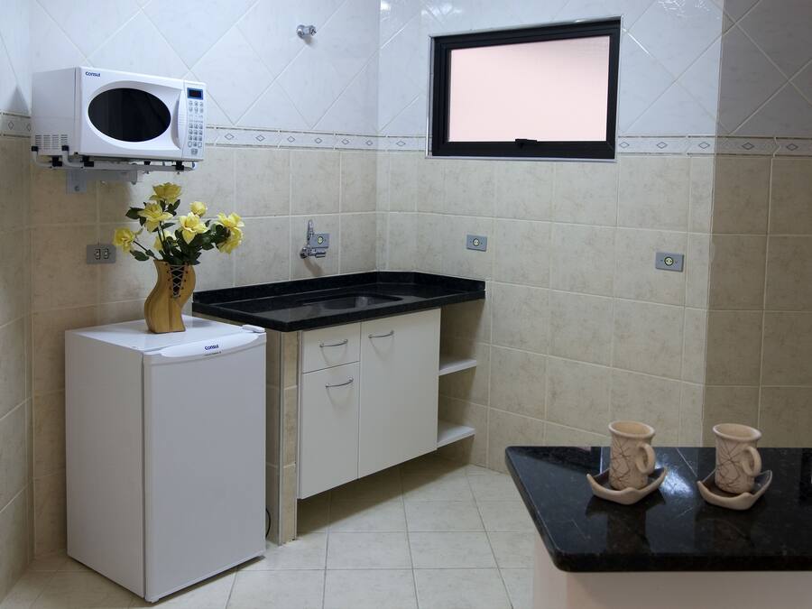 Una cocina compacta con microondas integrado, un lavamanos y una pequeña encimera.