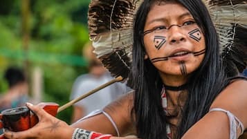 Una persona sosteniendo un objeto tradicional, vistiendo una prenda estampada y un tocado emplumado.