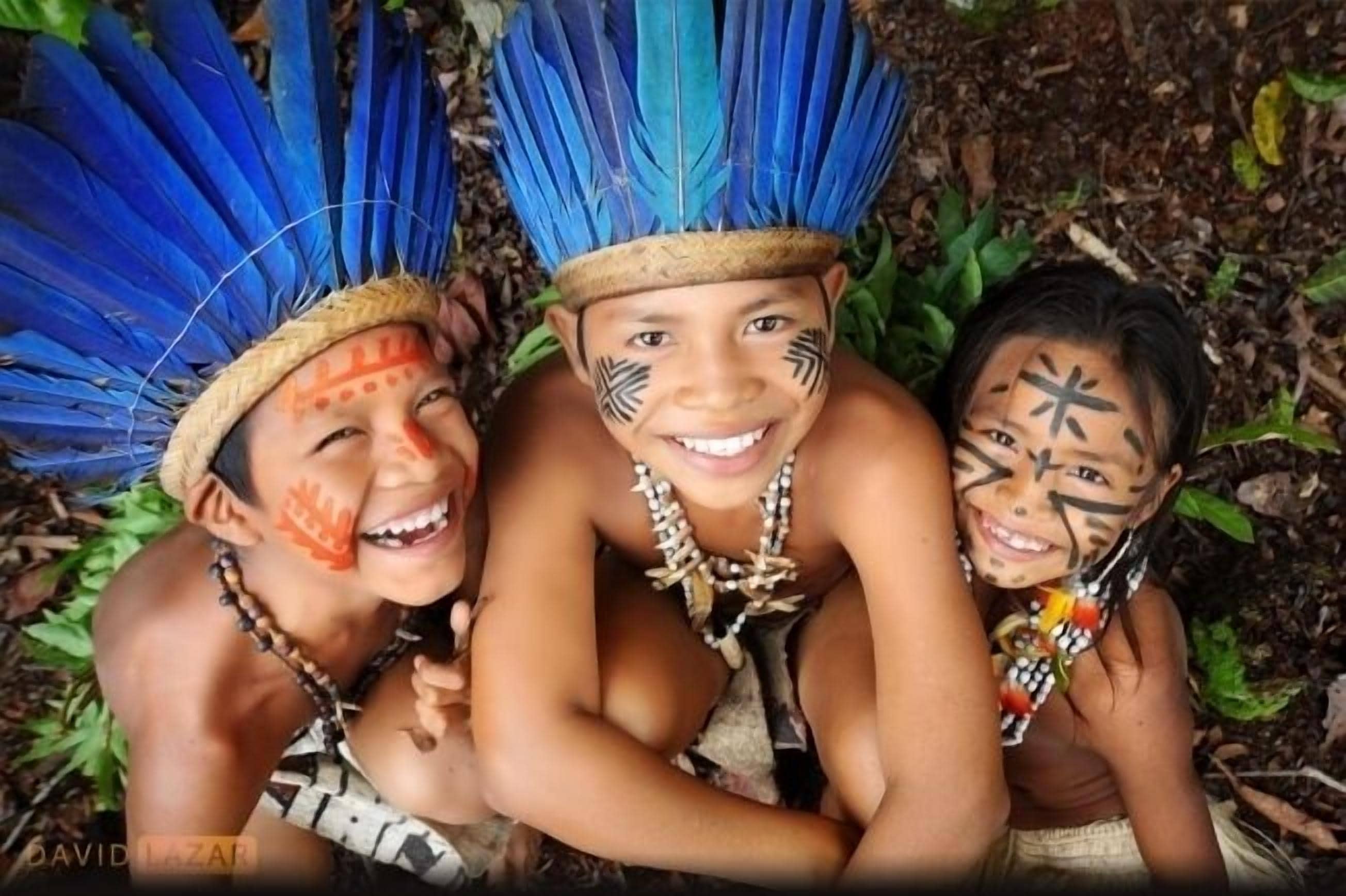 Three individuals wearing traditional attire with feathered headdresses and face paint.
