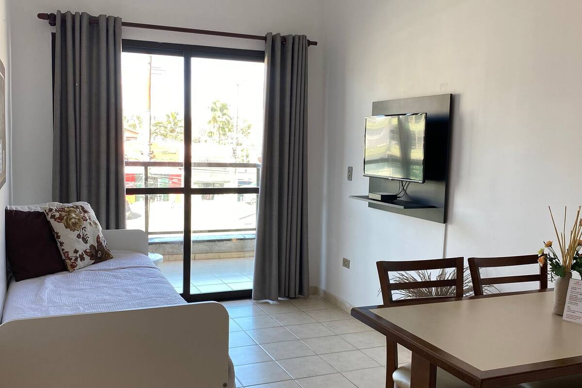 A hotel room with a bed, a dining table with chairs, a TV mounted on the wall, and a sliding glass door leading to an outdoor area.