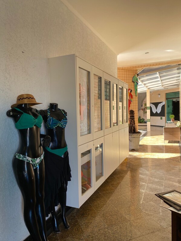 A hallway with a row of glass-fronted cabinets, a mannequin with a hat, and a wicker chair.