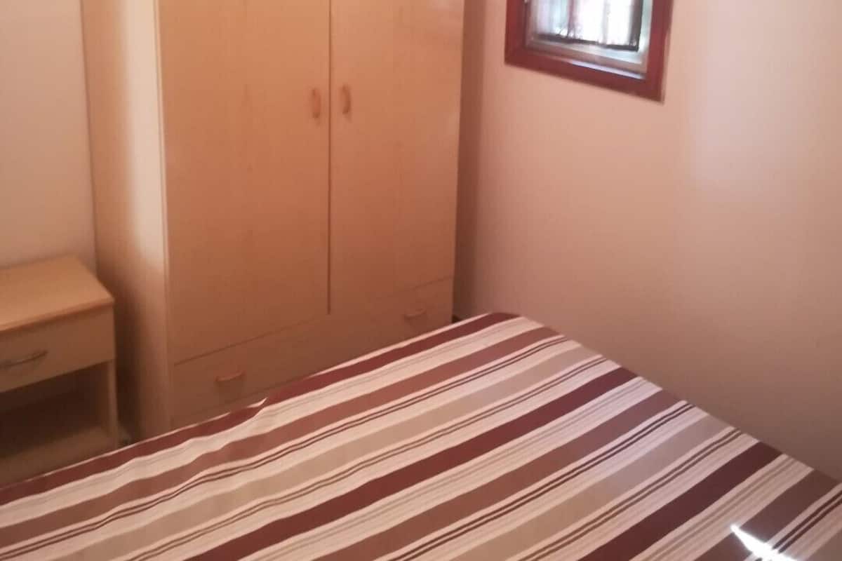 A bedroom with a bed, a wardrobe, a window, and a bedside table.