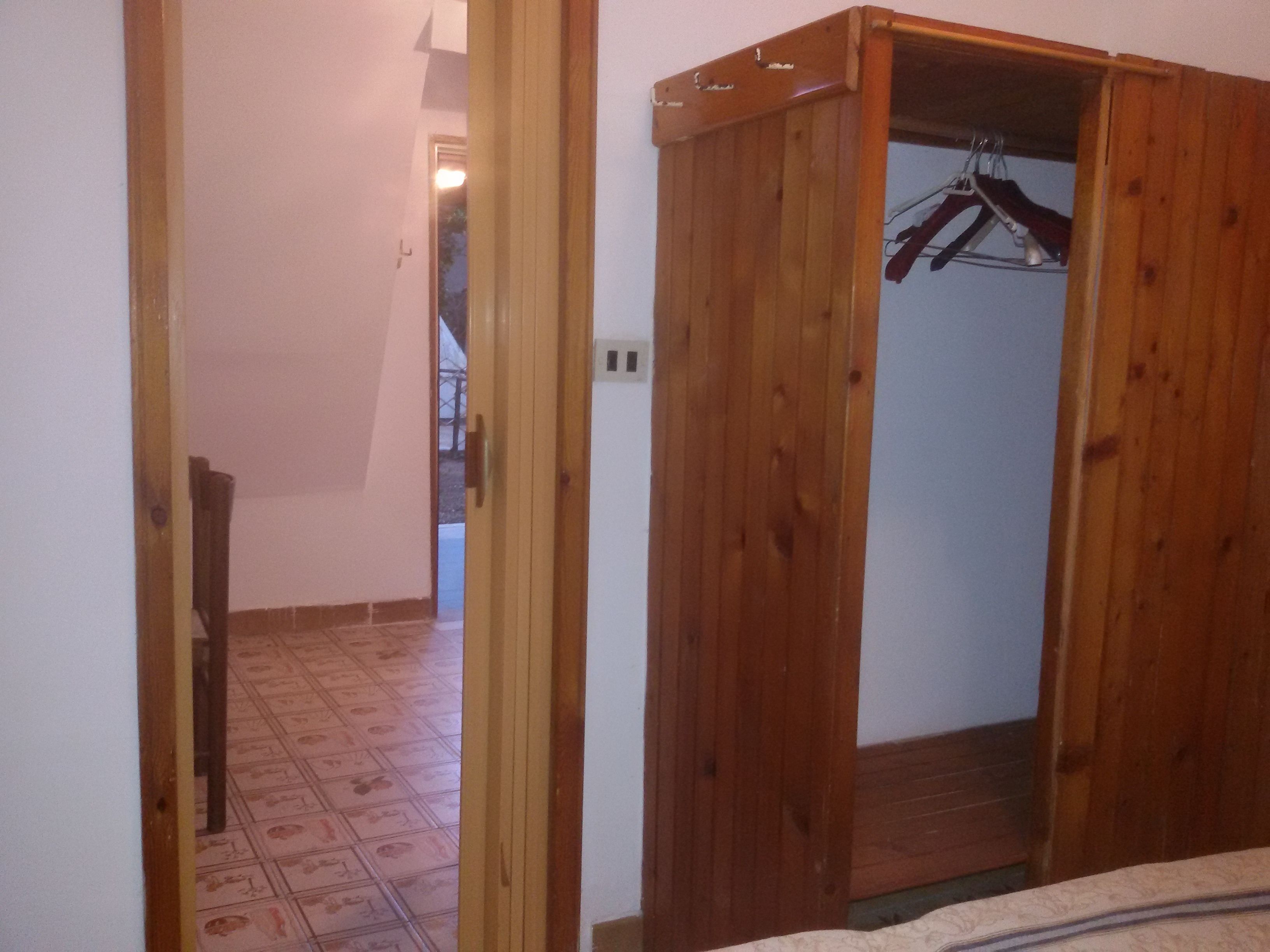 Un armario de madera con perchero, suelo de baldosas y una puerta que da a otra habitación.