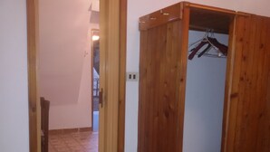 Ein Holzkleiderschrank mit Kleiderstange, gefliestem Boden und einer Tür zu einem anderen Raum.