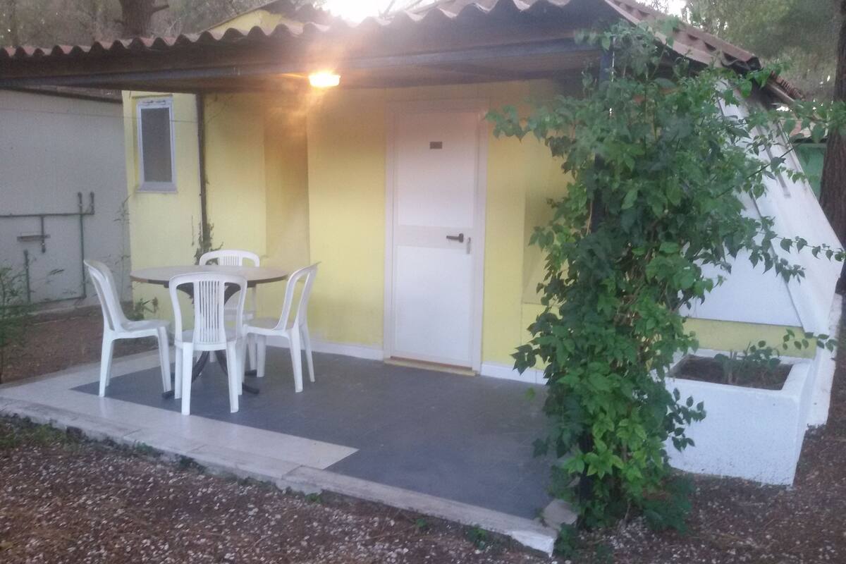 A small, single-story building with a yellow exterior and a white door. There is a table with four white chairs outside.