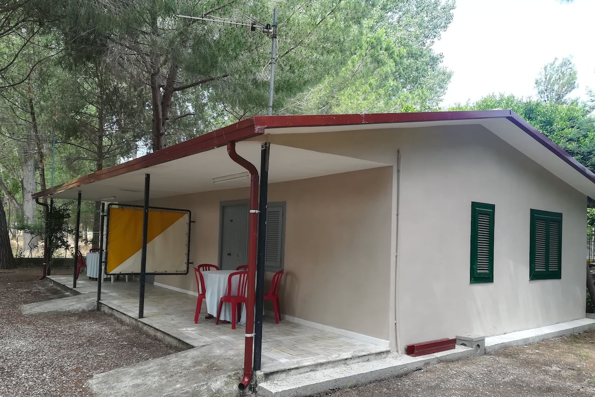 A small, single-story building with a covered patio area, a table with chairs, and a door with a window.