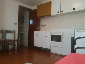 A kitchen with white cabinets, a stove, and a sink. There is a wooden chair and a red chair.