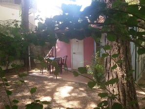 Eine Terrasse mit Tisch und Stühlen, einer Tür und einem Baum im Vordergrund.