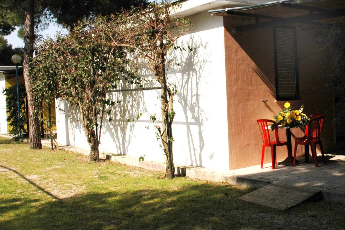 A patio area with a table and chairs, a small garden, and a white building with a brown wall.