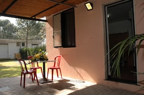 Eine Terrasse mit Tisch, Stühlen, einem Blumentopf und einer Glastür.