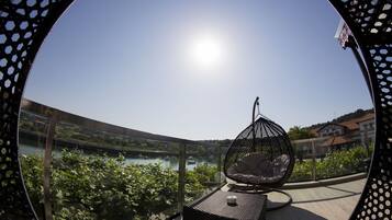 A balcony with a hanging chair, a view of a river, and a clear sky.