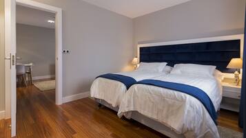A double bed with a dark headboard, two bedside tables with lamps, and a small desk with a chair in the adjacent room.
