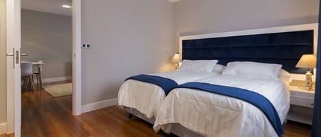 A double bed with a dark headboard, two bedside tables with lamps, and a small desk with a chair in the adjacent room.