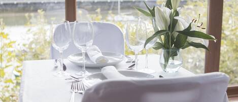 Una mesa lista para una comida, con vista a un río y colinas al fondo.