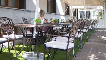 Un espace extérieur aménagé avec des tables et des chaises, une personne assise à une table et un bâtiment en arrière-plan.