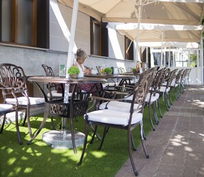 An outdoor seating area with tables and chairs, a person seated at a table, and a building in the background. - Hotel Boutique Bahía de Plentzia (Plencia)