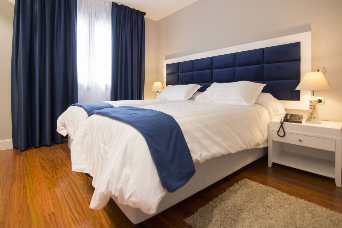 Una habitación de hotel con una cama grande, dos mesitas de noche y una mesilla.