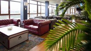 A spacious lobby with leather sofas, a vintage trunk, and large windows offering a view. - Hotel Boutique Bahía de Plentzia (Plencia)