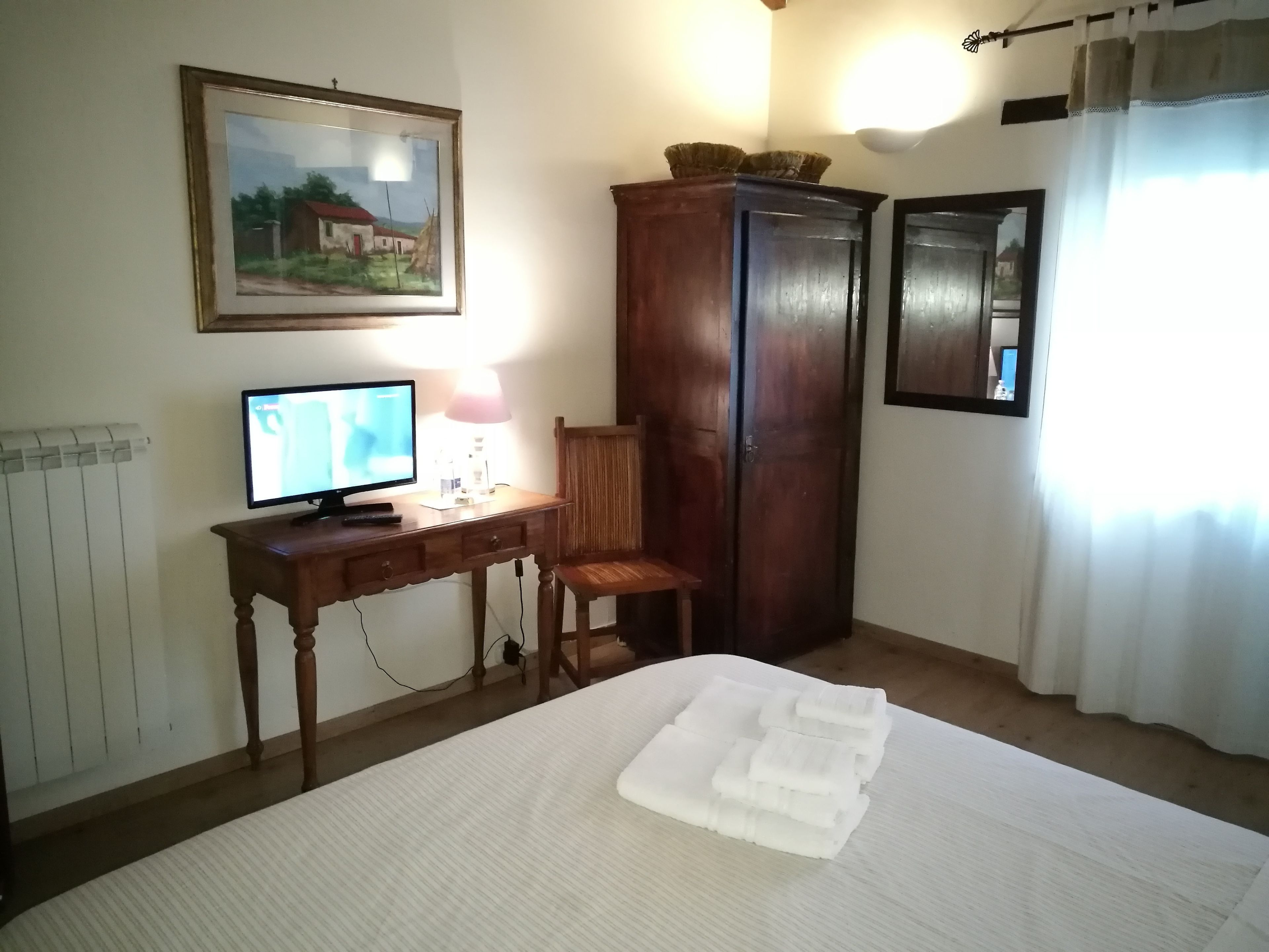Un dormitori amb un llit, escriptori amb ordinador, cadira, armari i un quadre a la paret.