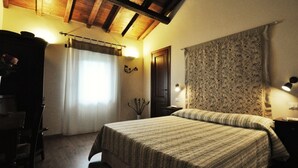 Une chambre à coucher avec un lit, des poutres en bois au plafond, une fenêtre avec des rideaux, une table de chevet et une lampe fixée au mur.