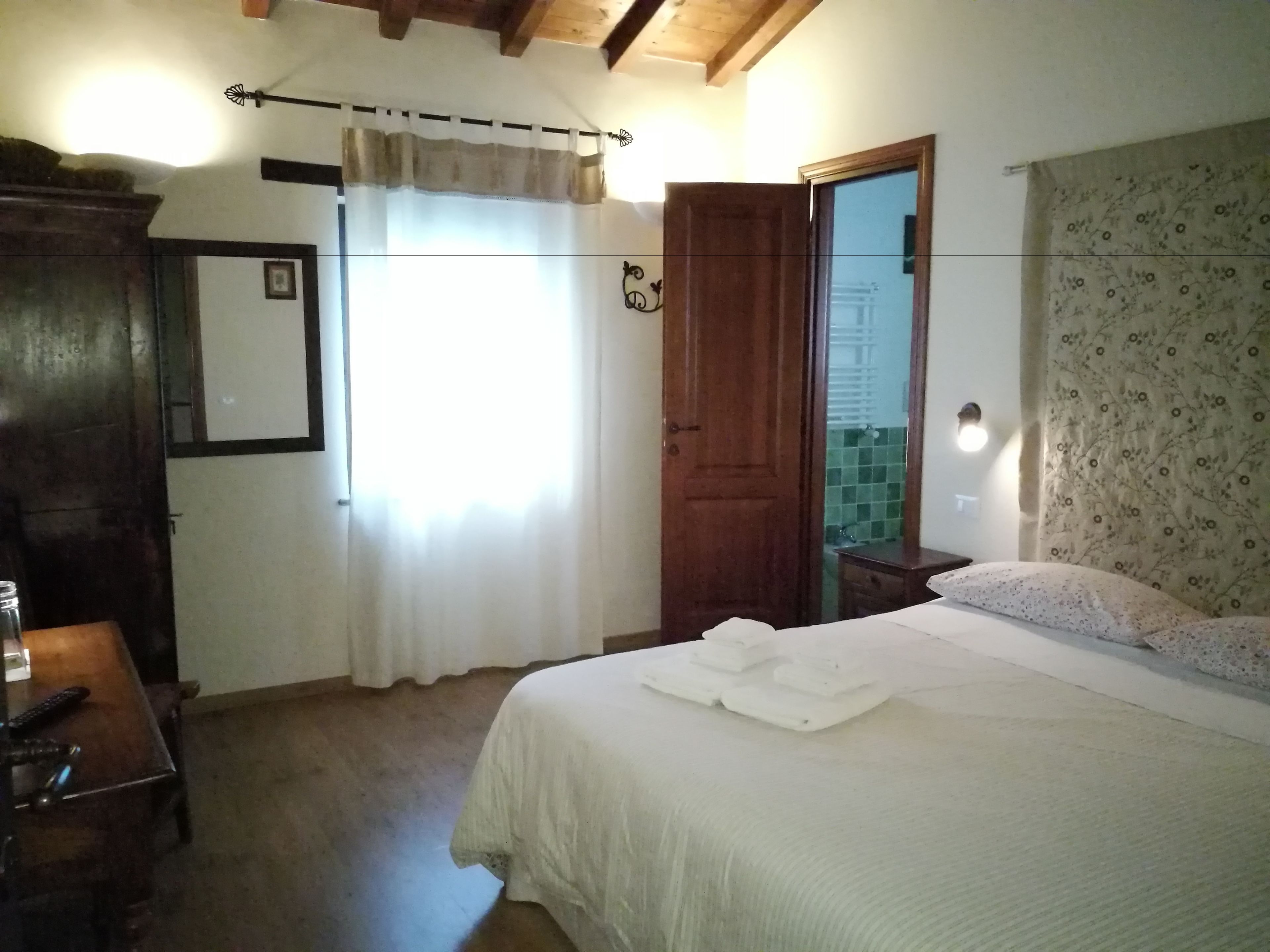 Un dormitorio con cama, un armario de madera, un escritorio con silla, un espejo y una puerta que da al baño.