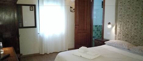 Un dormitorio con cama, un armario de madera, un escritorio con silla, un espejo y una puerta que da al baño.