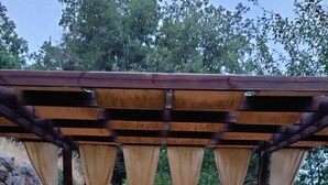 Un espace de restauration en plein air agrémenté d’une pergola en bois, de sièges confortables et d’une table dressée pour deux personnes.