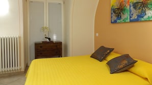 A bedroom with a yellow bedspread, a wooden dresser, a radiator, and a window with blinds. - Casa Portici (Torri del Benaco)