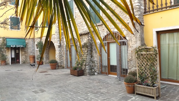 A courtyard with stone paving, potted plants, and a building with a 'BAR DAVID' sign. - Casa Portici (Torri del Benaco)