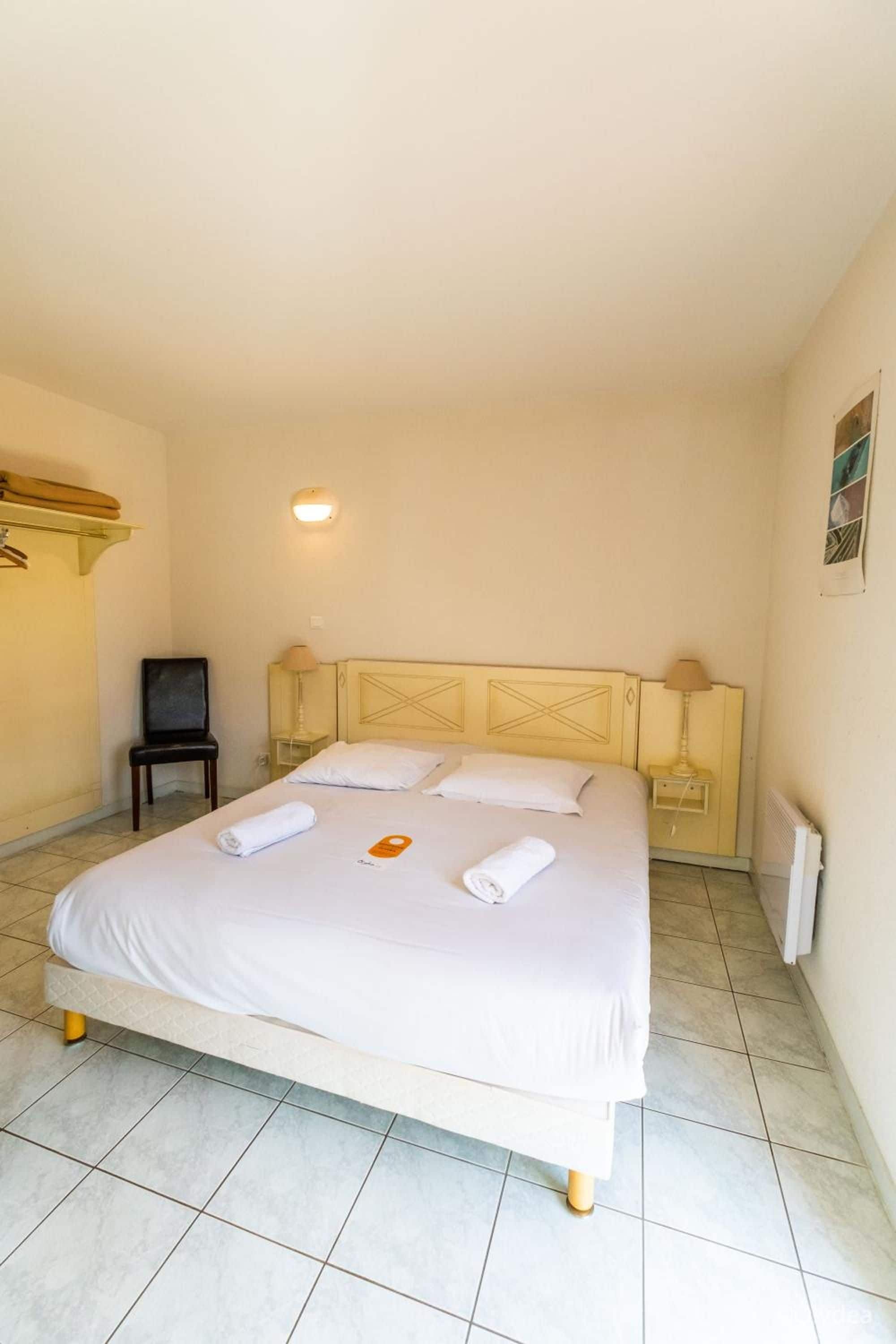 Een hotelkamer met een enkel bed, twee nachtkastjes, een stoel, een wandlamp en een radiator.