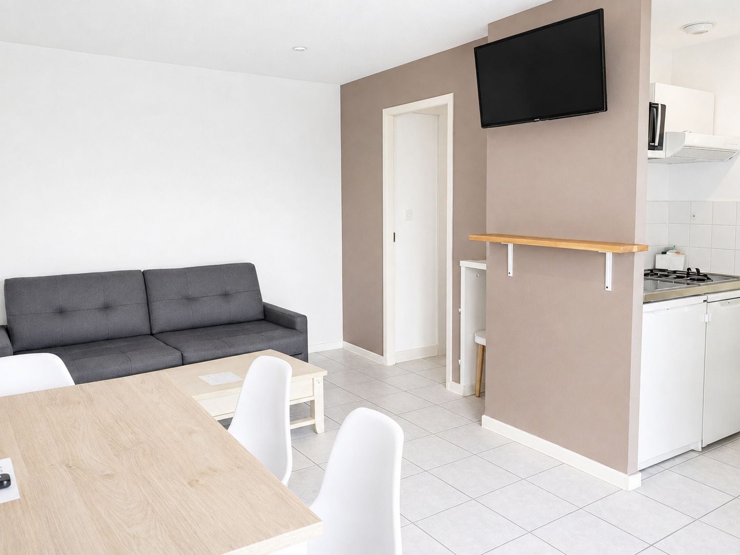 Un espacio habitable moderno con un sofá gris, una mesa de comedor de madera y una cocina con estufa y armarios blancos.