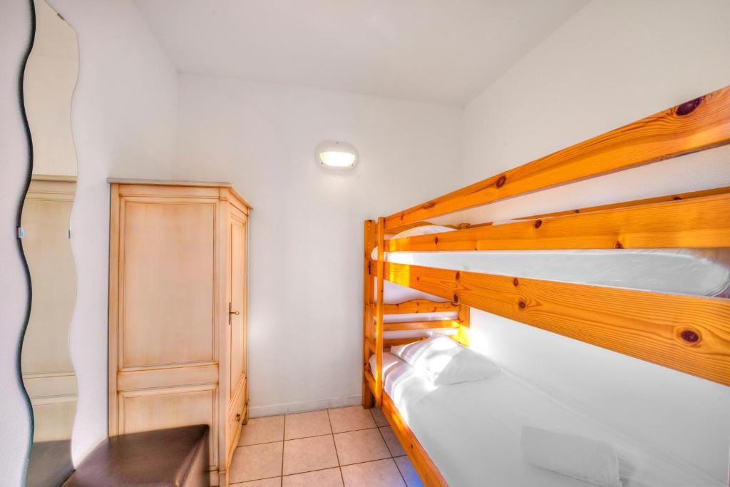 A bunk bed with a wooden headboard and a wardrobe in a room with white walls and a tiled floor.