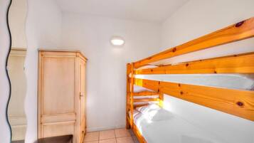A bunk bed with a wooden headboard and a wardrobe in a room with white walls and a tiled floor.
