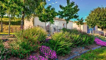 A residential property with a garden featuring various shrubs and flowers, a paved pathway, and a building with a tiled roof.