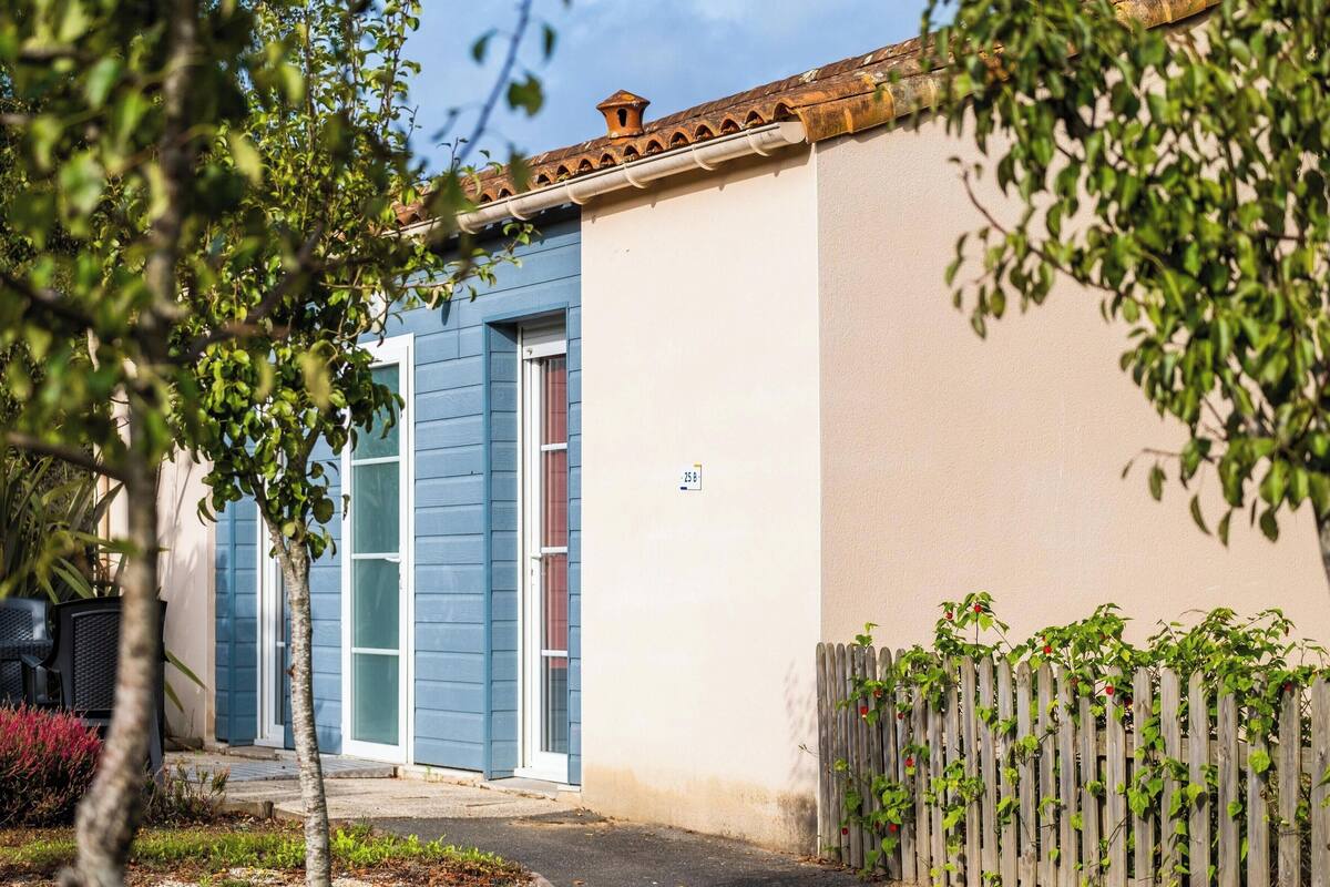 Un edificio residencial con una puerta azul, un pequeño jardín con plantas y una cerca de madera.