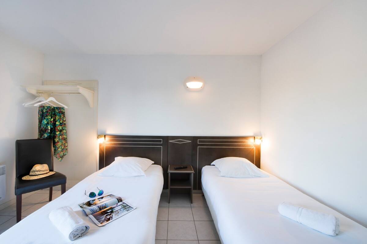 Habitación de hotel con dos camas individuales, una silla, una mesita y un perchero.