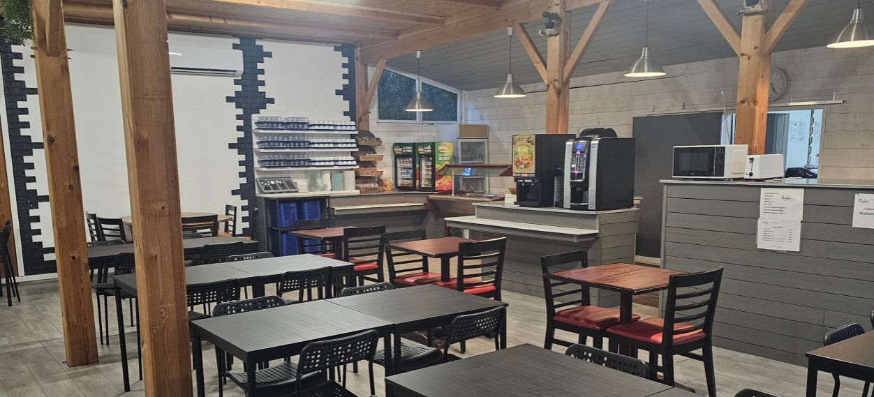 A restaurant with wooden beams, tables, chairs, a counter with a coffee machine, and a menu board.