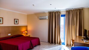 A hotel room with two beds, a desk, a chair, an air conditioning unit, and a window with curtains. - Hostal Casa Manolo (La Senia)